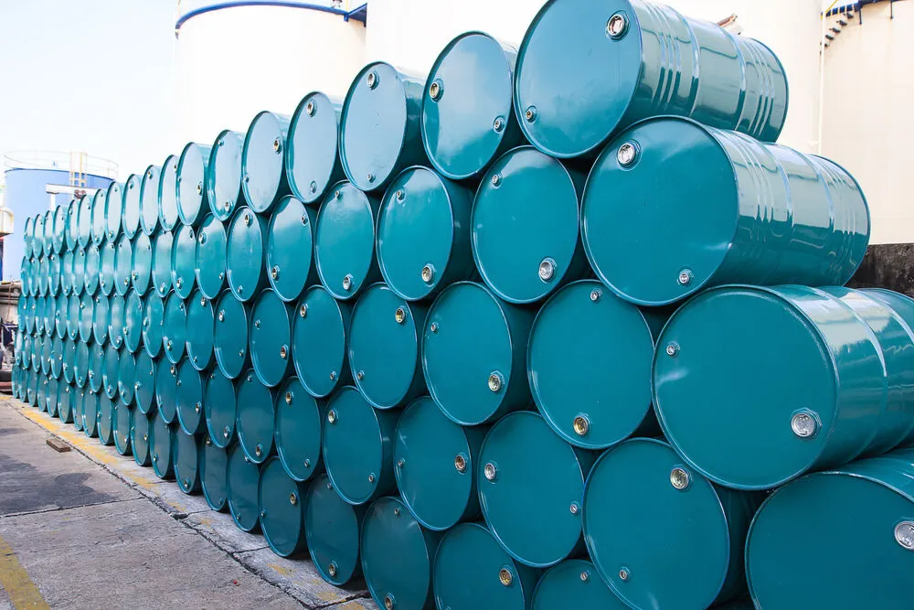 A large stack of teal-coloured metal oil drums organised in neat rows at an industrial facility.