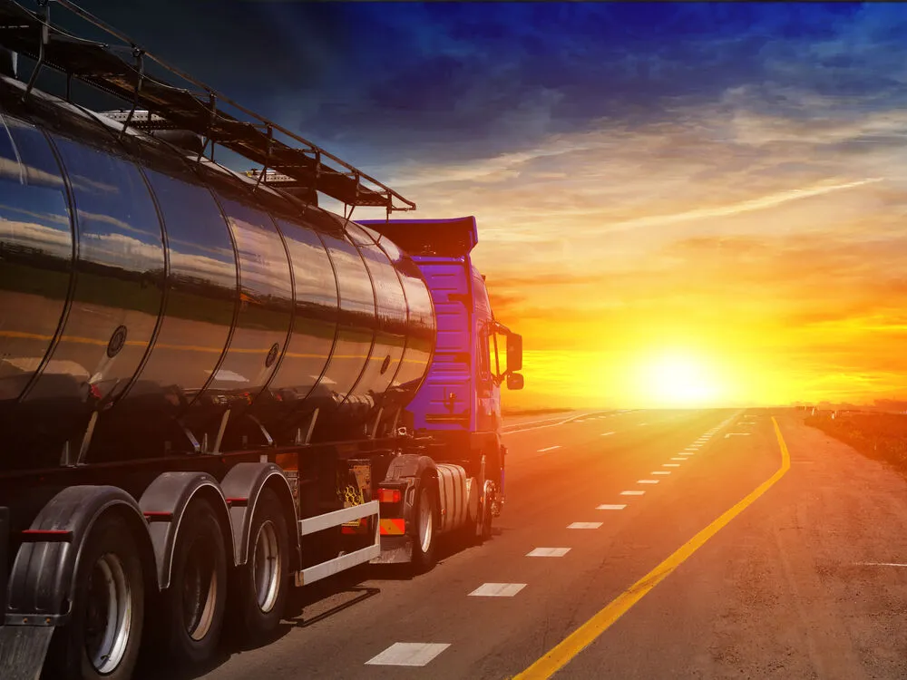 A blue semi-truck pulling a large, reflective silver tanker trailer travels along a highway