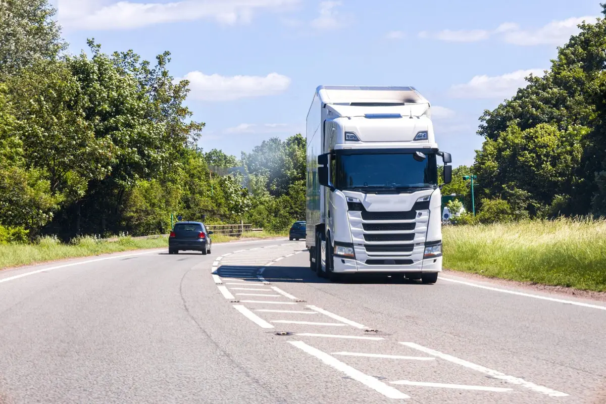 A large white semi-truck drives along a paved highway under a clear blue sky