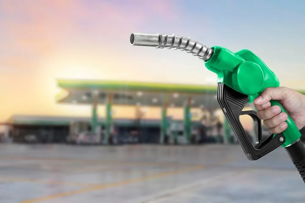 A hand holding a green fuel nozzle in the foreground