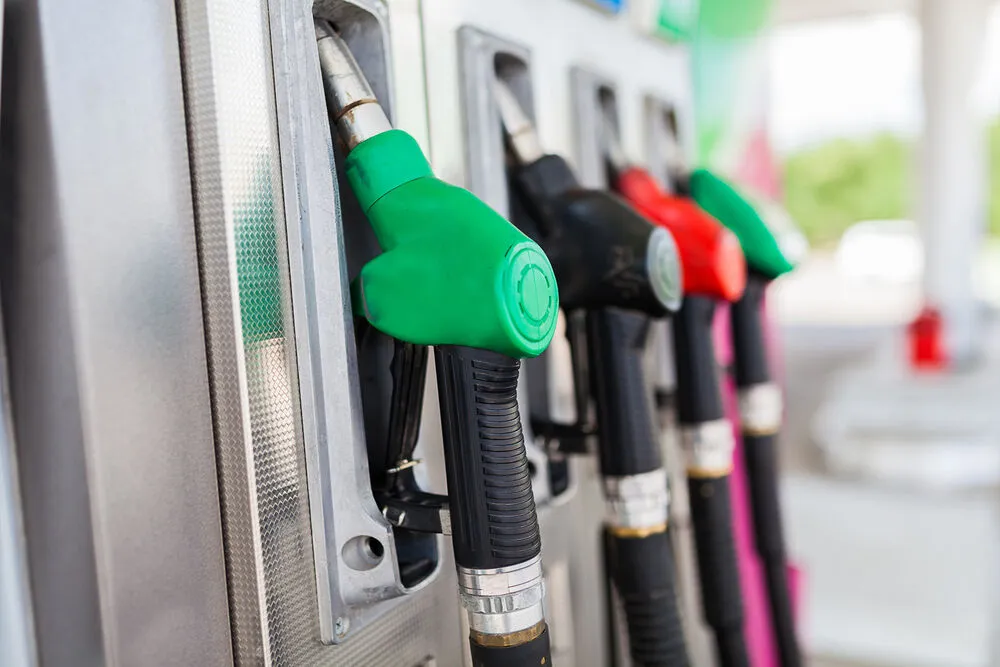 A row of colourful fuel nozzles, green, black, and red, resting in their holsters at a gas station pump.