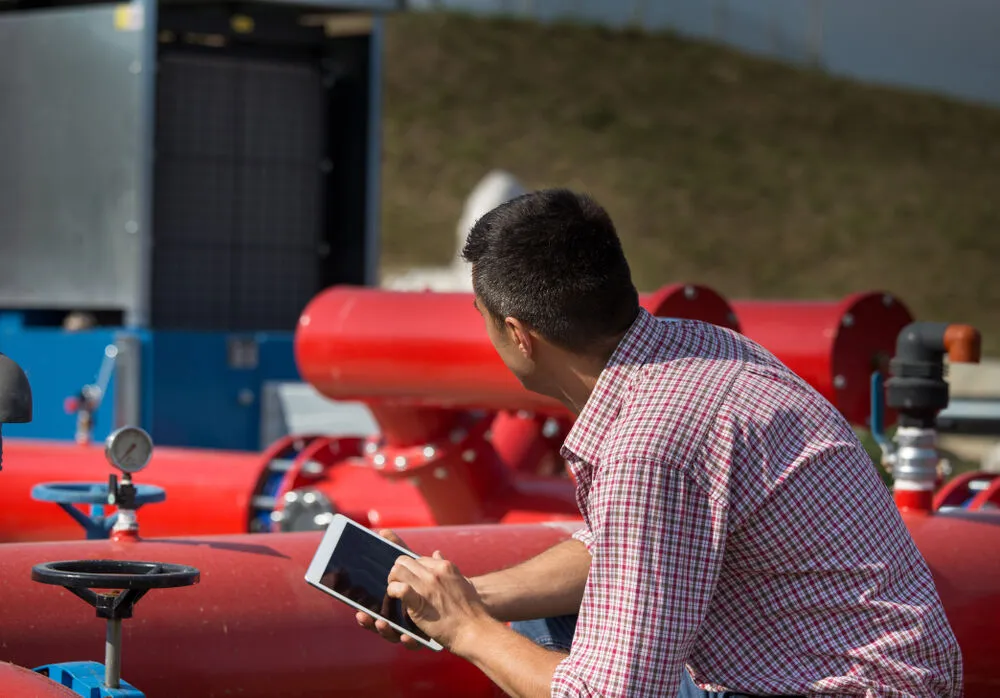 A man in a plaid shirt kneels outdoors at an industrial site