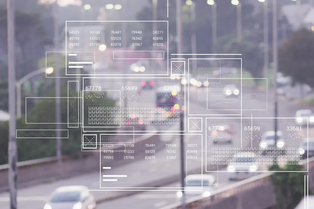 A high-angle view of city traffic on a highway overlaid with crisp white digital graphics, including data grids, charts, and numeric panels.