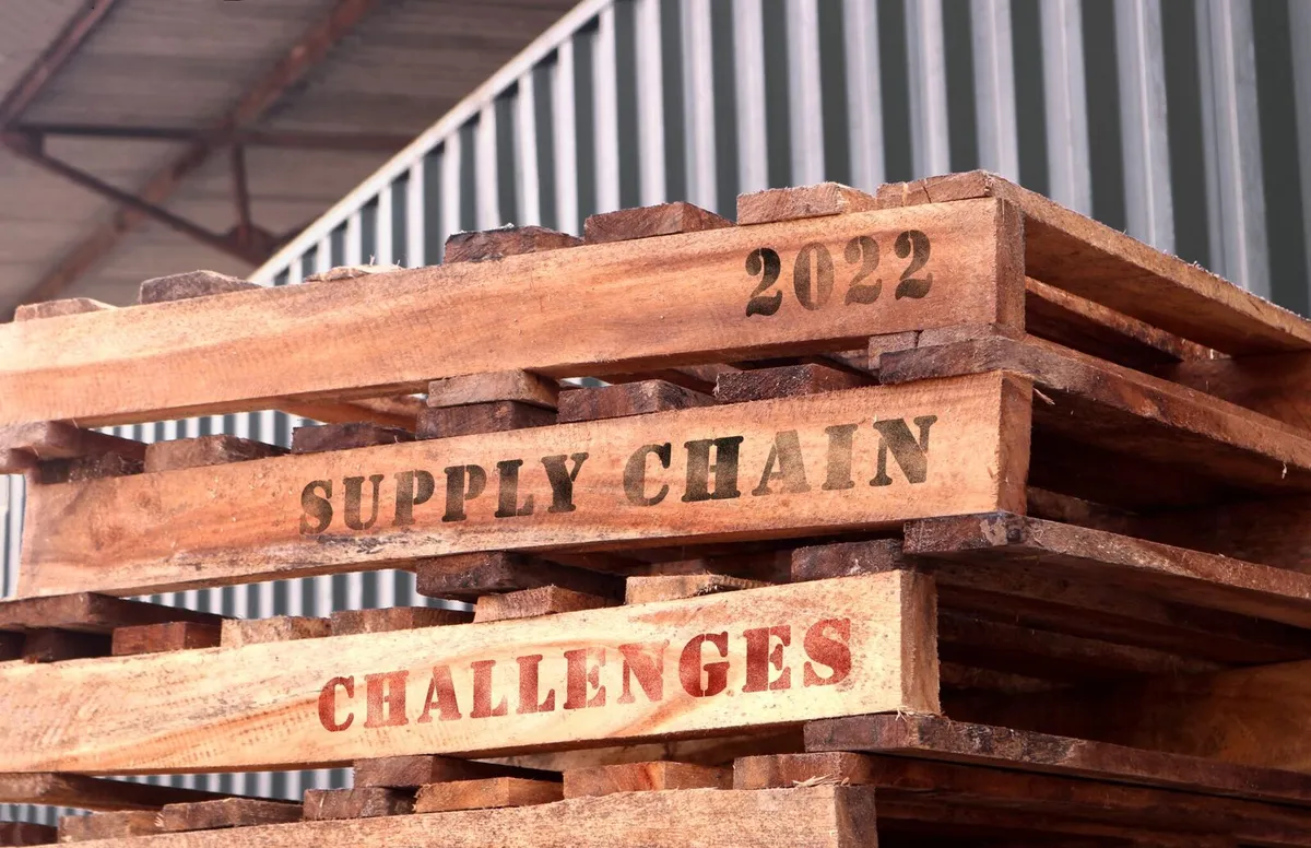 A stack of wooden pallets with the words "2022 SUPPLY CHAIN CHALLENGES" printed on the side slats.