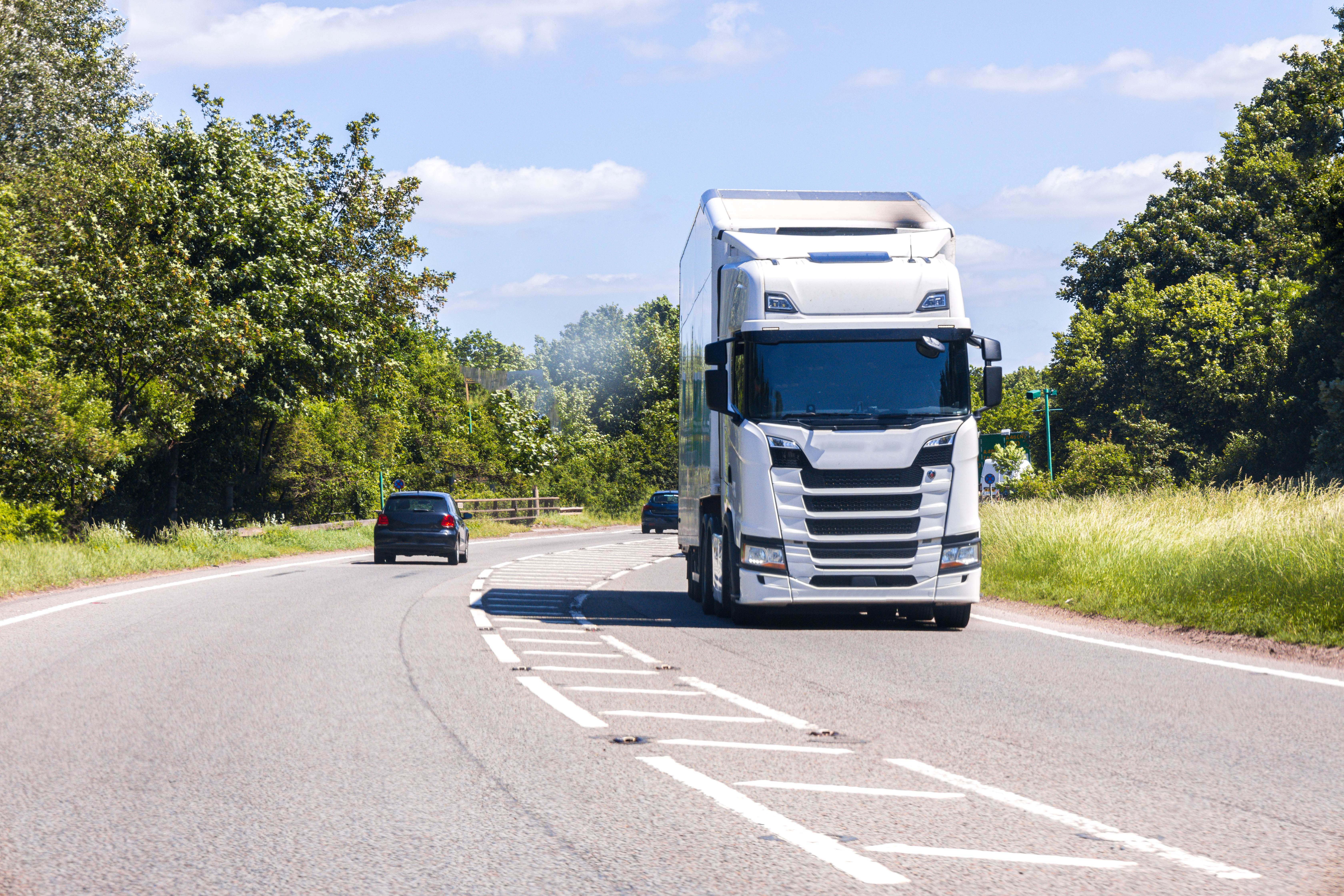 A large white semi-truck drives along a paved highway under a clear blue sky