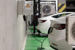 An electric vehicle (EV) charging station in an indoor parking garage, with a white car plugged into a wall-mounted power box.